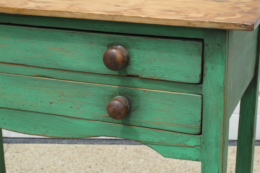 A small painted English table with natural pine top and two drawers, with wooden pulls.
