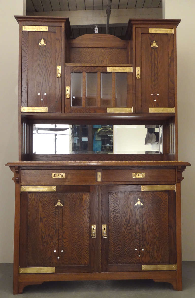 A Southern German Secessionist period two part cabinet whose design is attributed to Koloman Moser; executed in oak; having doors in both upper and lower sections inlaid with period motifs rendered in brass, ebony and mother-of-pearl; the upper