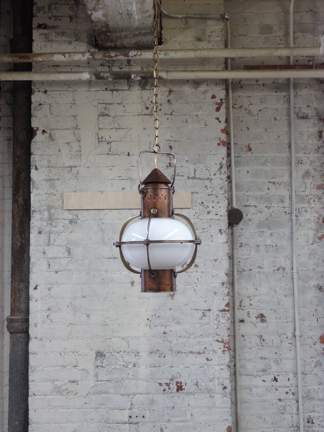 An English Arts & Crafts style hanging lantern executed in brass and copper with a milk glass shade. Unwired. Chain and canopy not included. Four lanterns available.