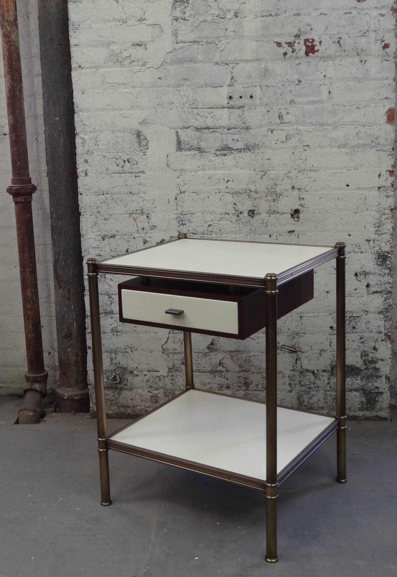 The Cole Porter style side table, two shelves wrapped in parchment with a floating drawer mounted beneath the top shelf, the drawer face also wrapped in parchment, all held in a patinated brass frame with custom brass edge molding. Design inspired