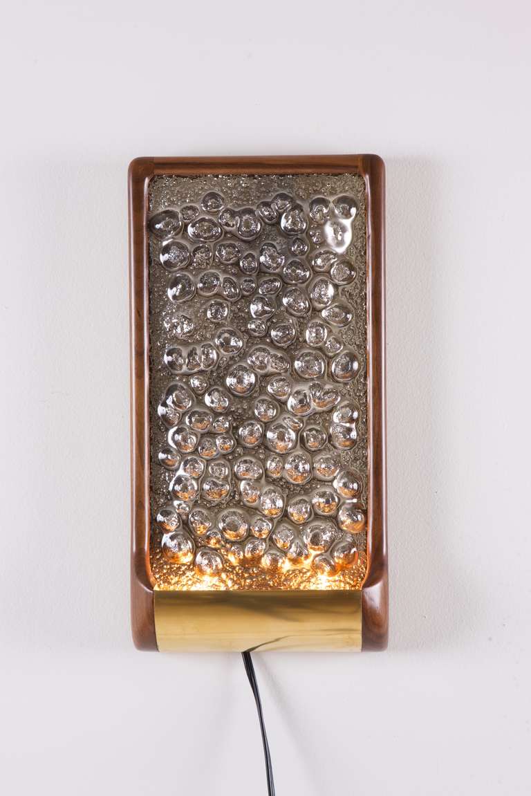 A mirrored wall sconce by Victoria & Son with a textured and irregular convex surface, each handcrafted and unique, surrounded by a American walnut frame with brass detail. Supplied wired with two halogen bulbs. Also available not wired or UL wired
