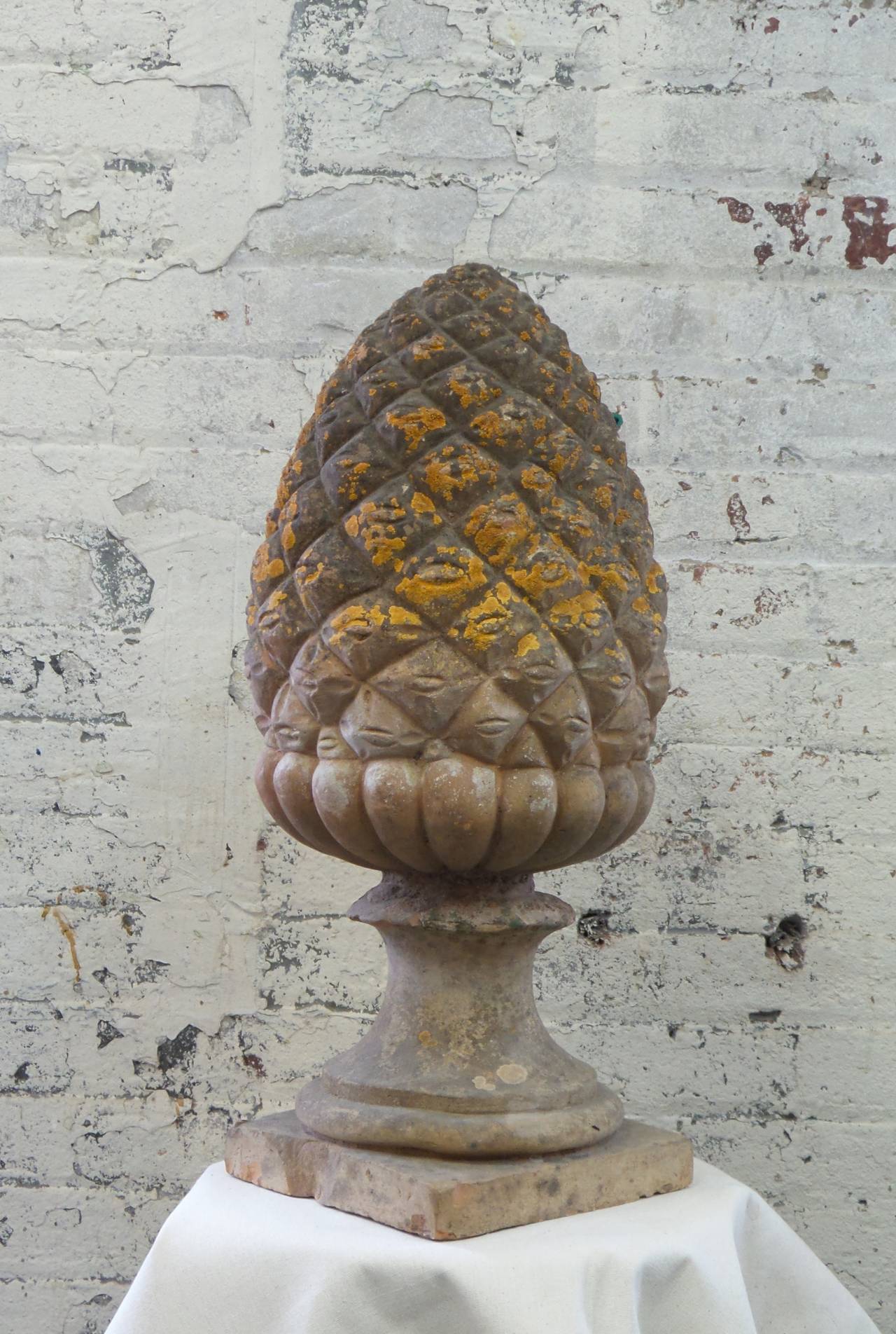A finely modeled terracotta pine cone finial used as a garden ornament with naturally occurring patina.