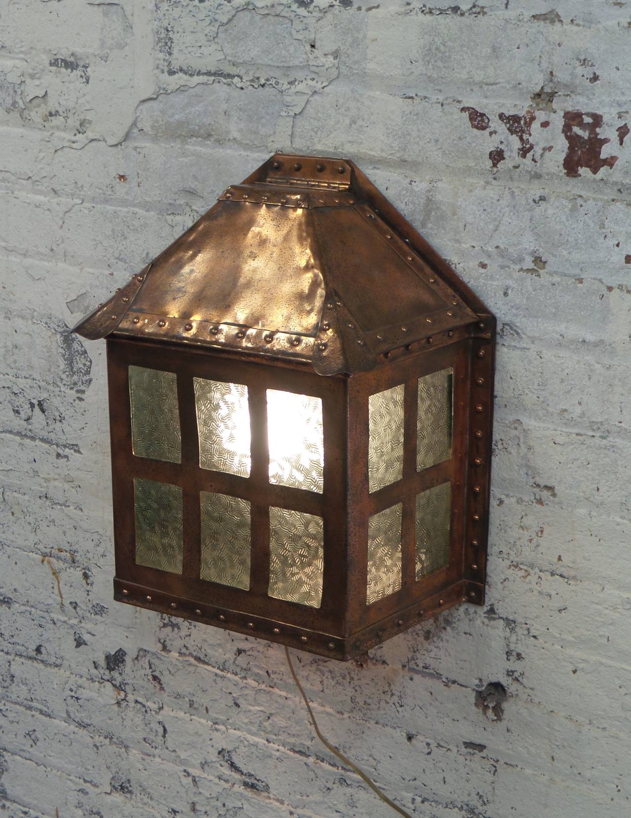 An English Arts and Crafts copper wall light with exposed riveted metal construction detail and green textured glass insets on the front, sides and bottom surface. Wired with one standard socket.