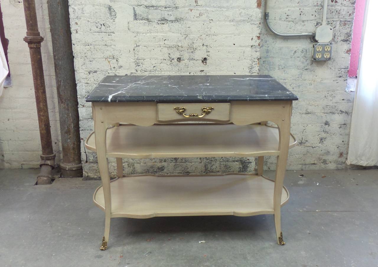 Astor model Louis XV style night table with three drawers, two shelves and shown with a nero marquina slab marble top and patinated brass pulls and sabot. Based on the design for Brooke Astor by Victoria & Son. Custom versions and finishes