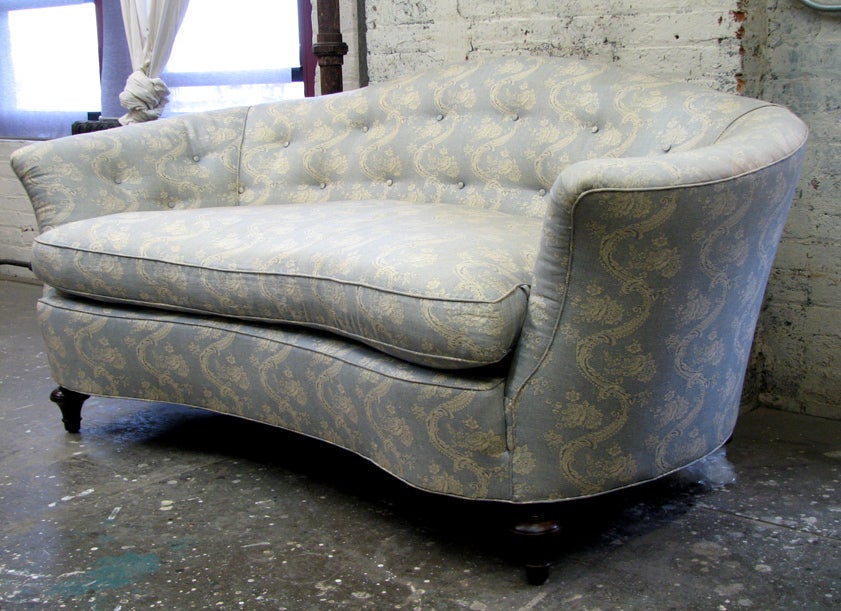 A small Victorian style sofa with wrap around arms, molded camel back, overall kidney shape with tufted upholstery.