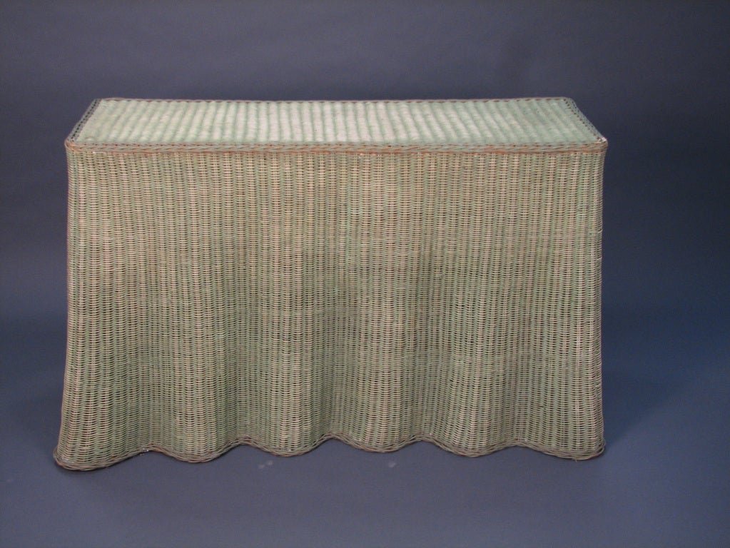 A faded green painted wicker console table with an undulating, wavy skirt form base, American circa 1970.