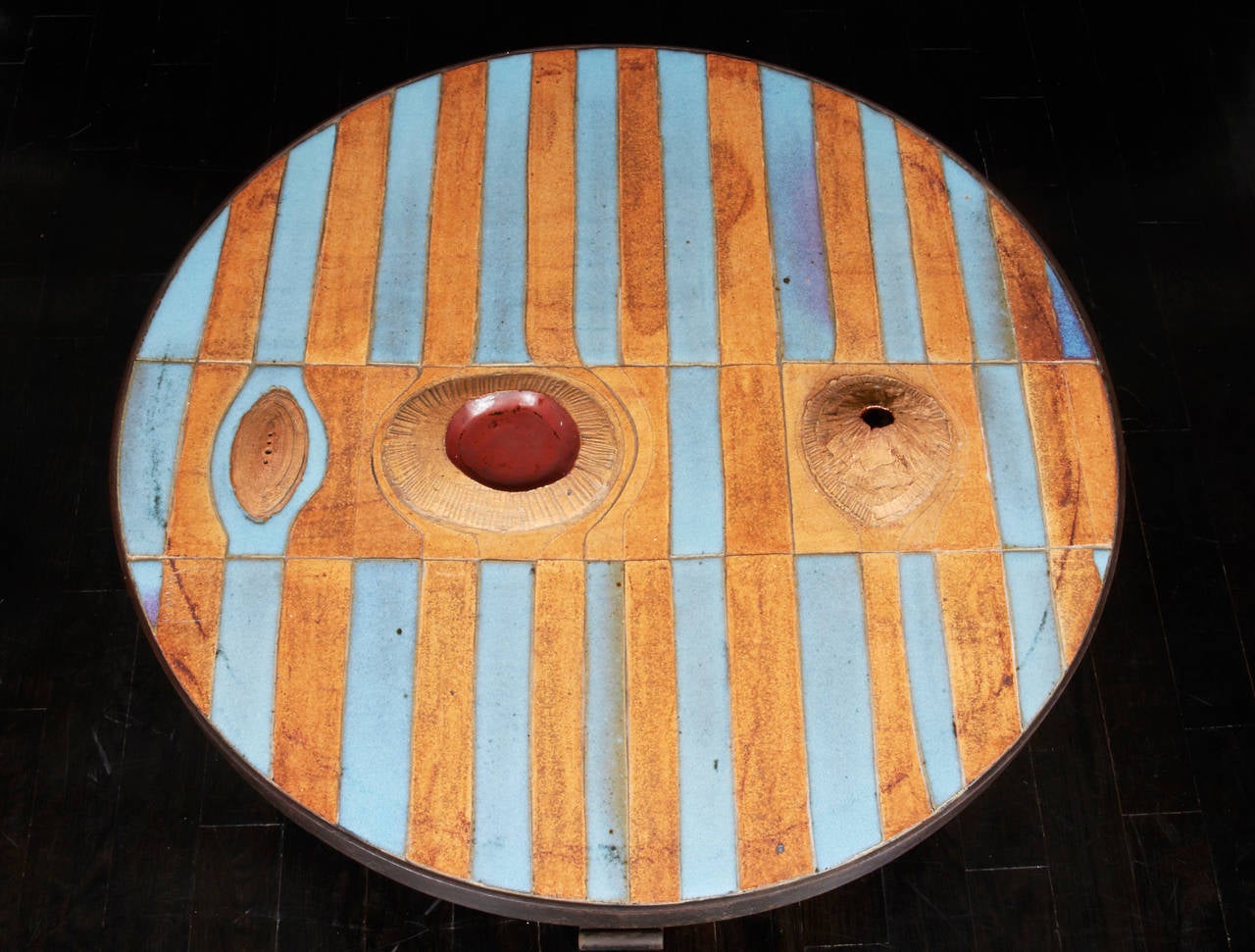 In the style of Pia Manu, a table top designed with stripes of blue ceramic mixed with terra-cotta set in a hand wrought bronze base. The red enamel and “volcano” details are in relief.