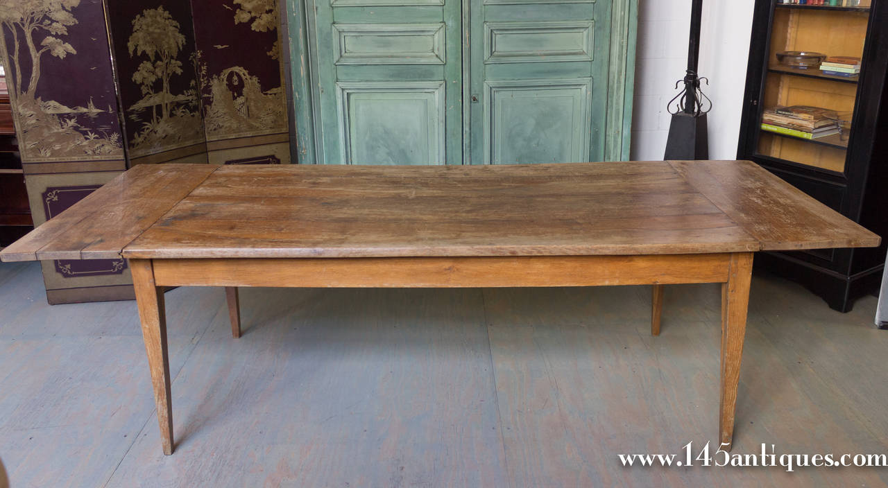 Very large French oak farm table with one-drawer. The end leaves have been permanently attached. The tabletop could be sanded down and waxed, or have a clear coat of poly to make it resilient to everyday use.