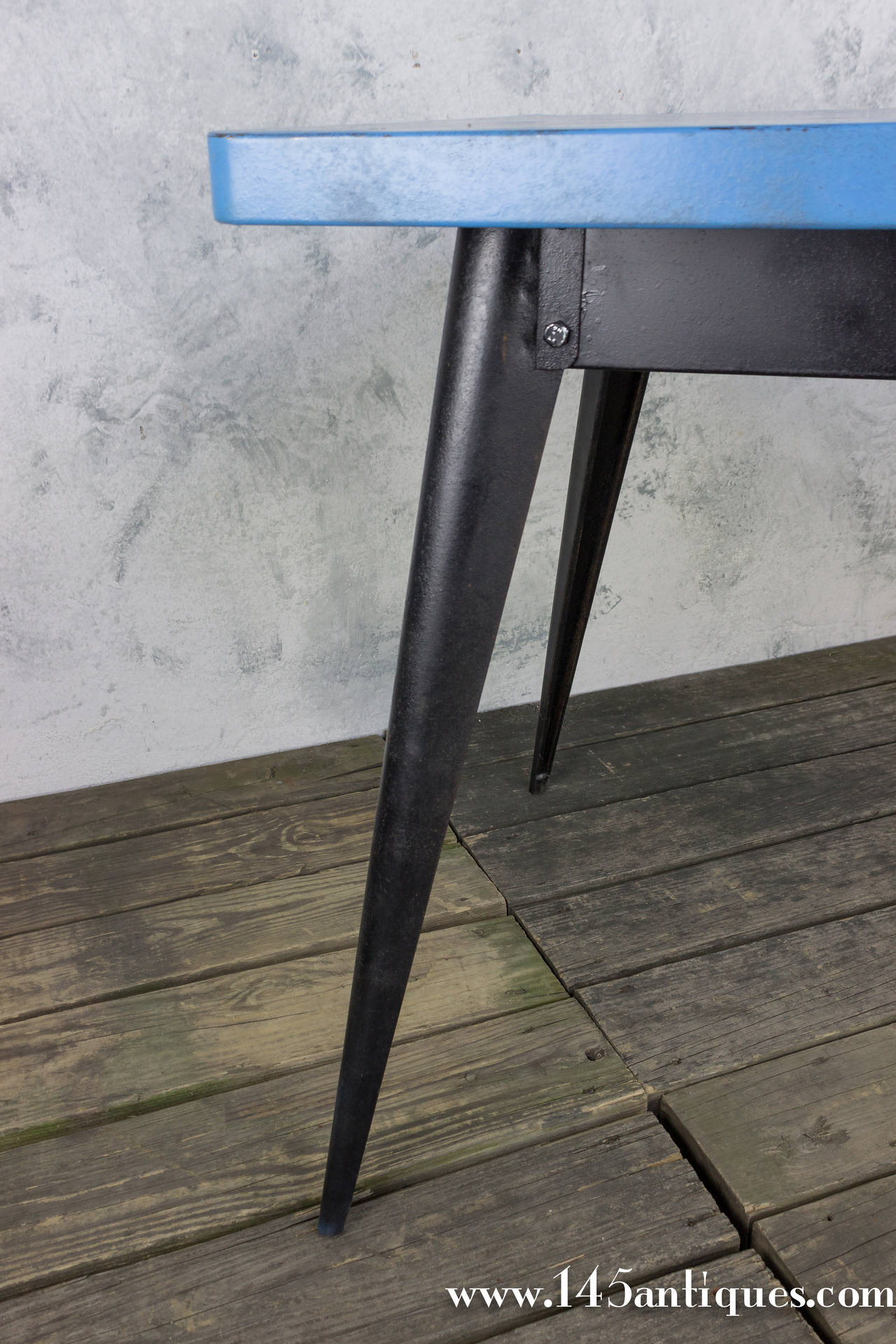 French metal table manufactured by the Tolix company, circa 1950. This table has a black painted base and a blue metal top.