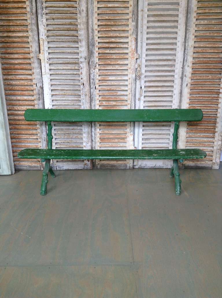 French late 19th century park bench in distressed green paint. Legs are in cast iron.

