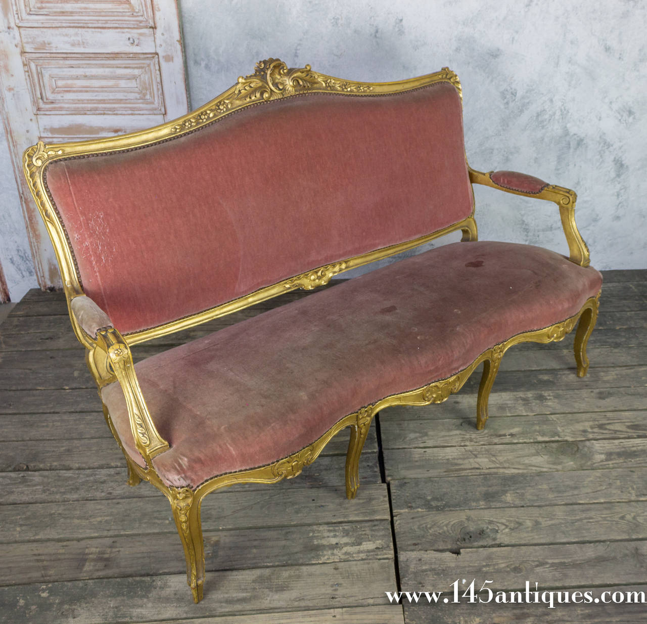 Late 19th century French settee in a painted gold finish and hand-carved decorations. The faded velvet is a deep salmon colored (needs to be replaced) This settee is part of a set, consisting of the settee, a pair of armchairs and a pair of side