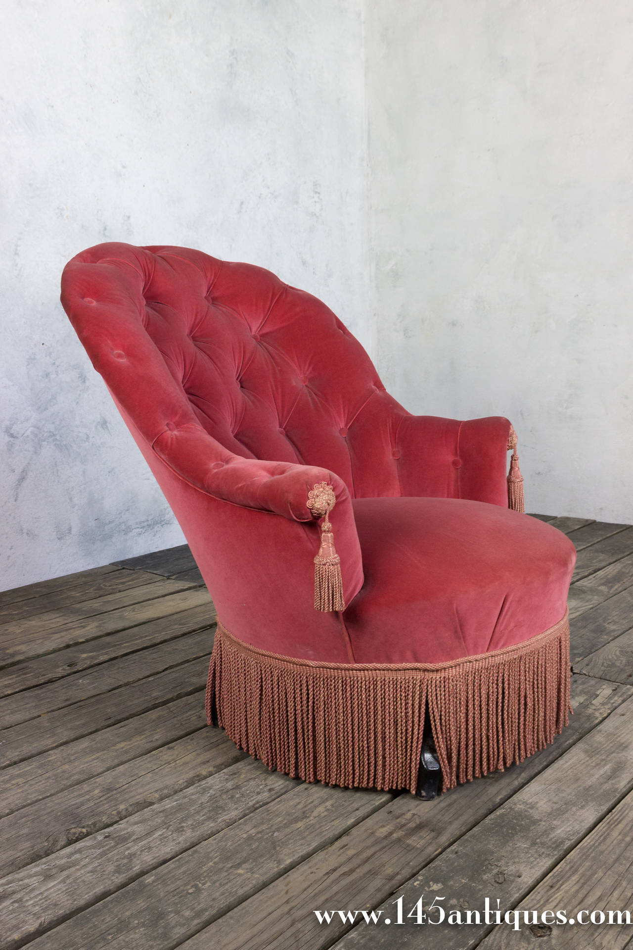 French Napoleon III style tufted armchair with a curved back. The chair has a great pitch making this an extremely comfortable chair. Upholstered in rose colored velvet with matching bouillon fringe.