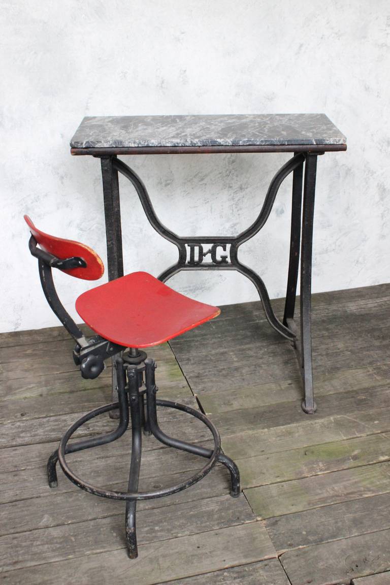 French 1920s iron base factory table with decorative "D G" on center support bars. The top of table is wood with a slab of marble placed on top.
