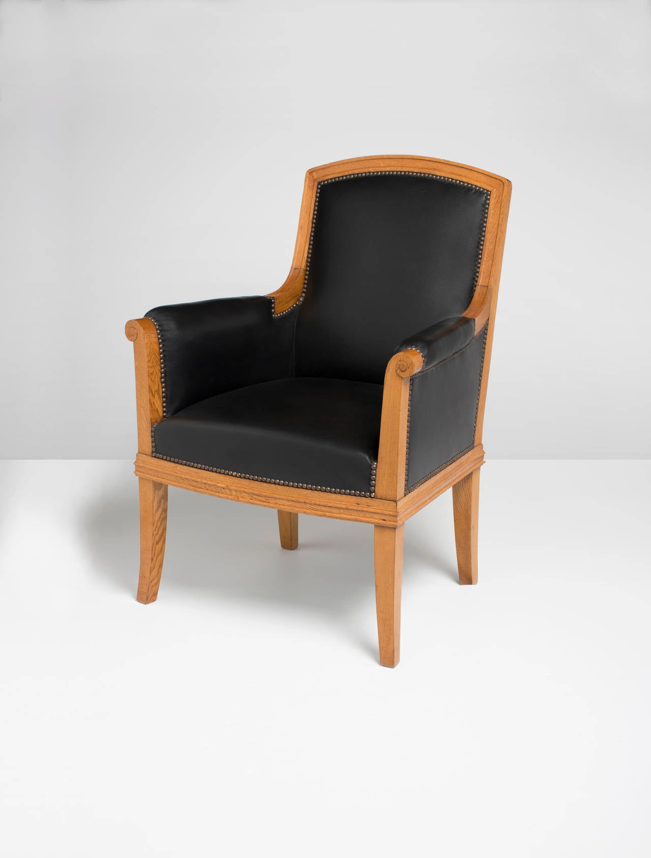 Este sillón presenta un elemento distintivo en los remaches de acero que adornan los puntos en los que la tapicería de cuero se une a la estructura de roble. 