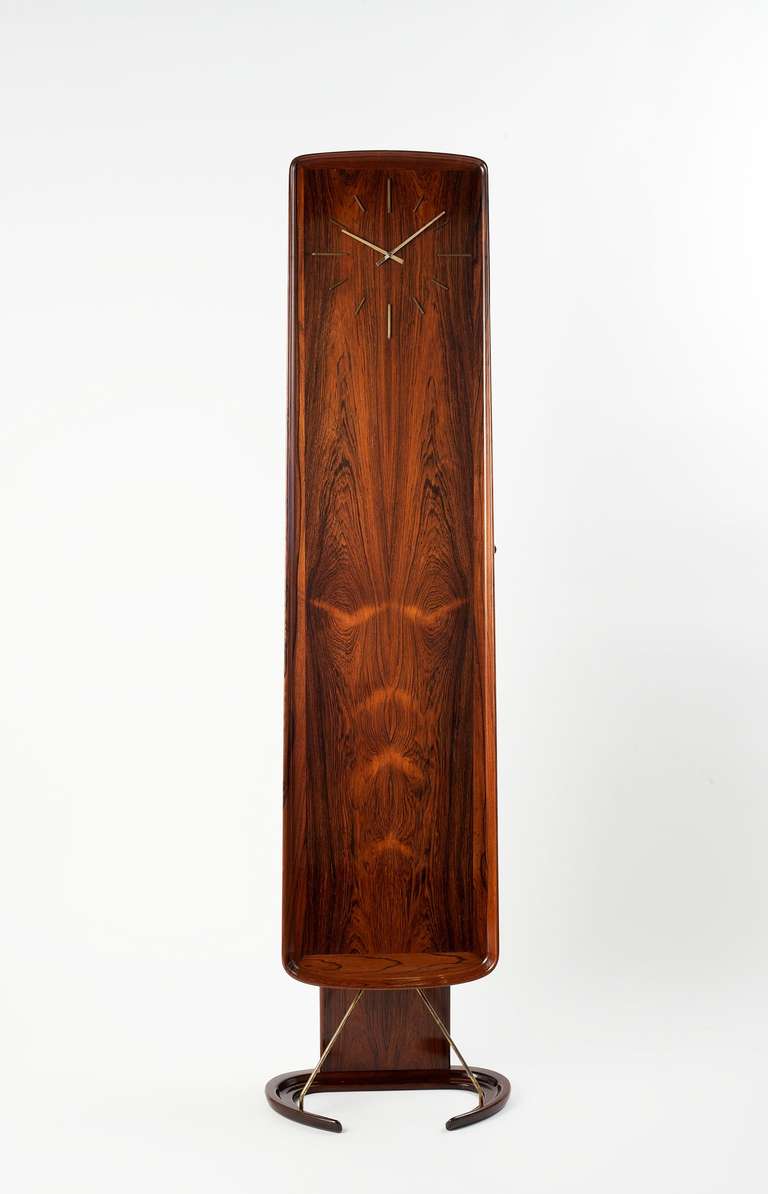 Olsen's remarkable mahogany grandfather clock, which rests upon a base shaped like a pair of devilish horns, doubles, with its numerous interior shelves, as a case piece.  

This marvelous work from the 1960s also bears its original metal plaque,
