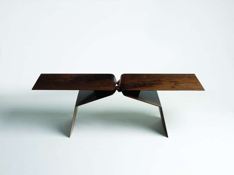 Cette table sculpturale taillée à la main fait partie d'une ligne de mobilier contemporain conçue en associant la technologie numérique à un artisanat traditionnel de qualité. Sculptée en noyer, la pièce présente deux contreforts entrecroisés qui,
