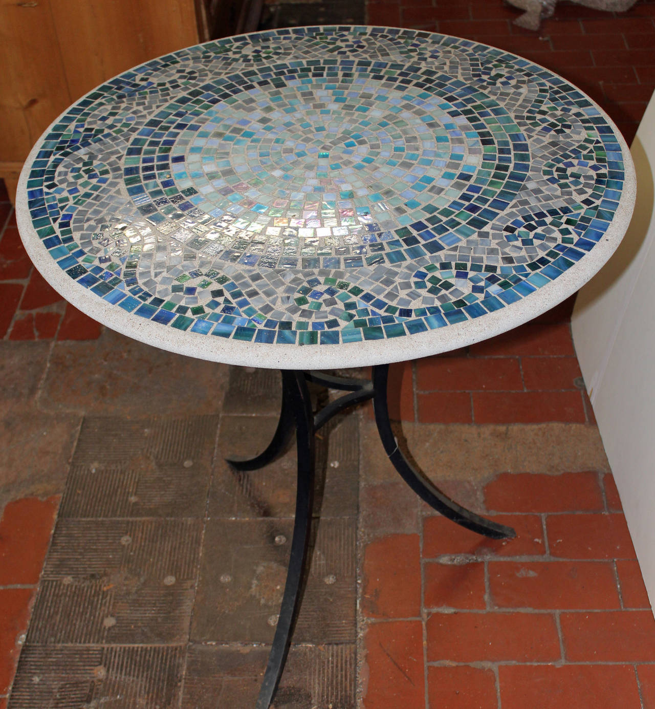 Whimsical mosaic breakfast table on blackened cast iron base.  The iridescent mosaic tiles are set in a sanded concrete.  The tri-legged base is in blackened steel