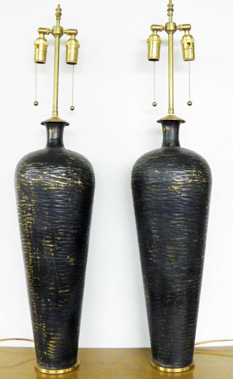 Large and elegant pair of textured gold and graphite metal vases with lamp application. The lamps are set on solid brushed brass plinths. The hardware is in polished brass. The dual-sockets are individually controlled. The finial post extends an