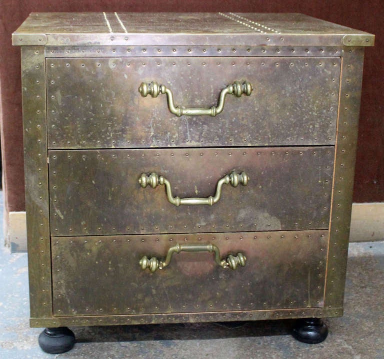 This 3 drawer cabinet is covered in brass with tack details and ebonized wood feet