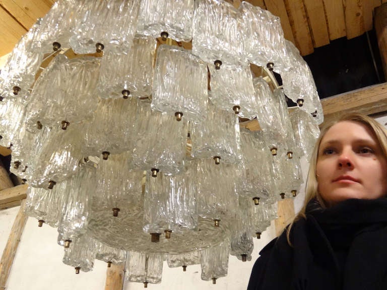 A large chandelier consisting of multiple pieces of textured glass hung from a brass frame with textured plate at bottom by Venini.

Italian, circa 1960s.

Five (5) chandeliers available.

25-40 Wattage Per Socket

14 Sockets

Type of Bulb: E14