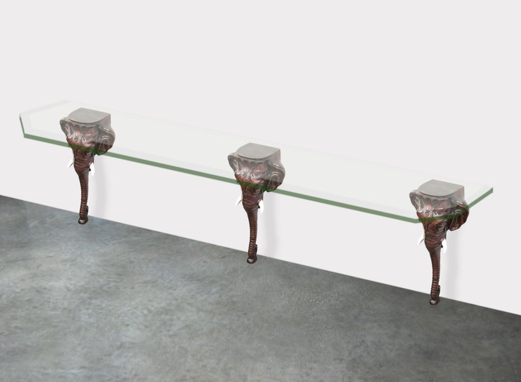 Console table with three Sabu hand-carved wooden elephant heads and long glass top, American, 1970s.
