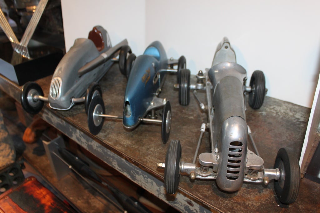 These cars could achieve speeds upwards of 70 miles an hour. The sport originated in the 1930's. Hobbyist would race for personal best times on a circular race track. The cars were controlled by a wire tether. These 3 cars are in original stock