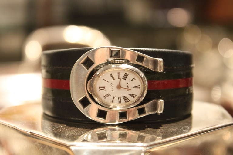 This is an extremely rare example of a 1970's Gucci watch. The Horseshoe form case is sterling and is the clasp for the opening and closing of the watch. The band is leather turned over steel with the famous green red stripes in patent leather. The
