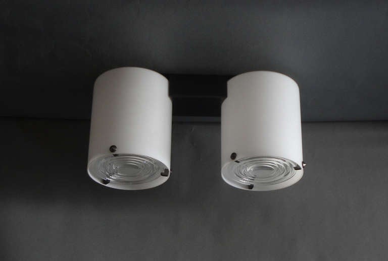 Fine French 1950s flush mount fixture by Jean Perzel with a black lacquered metal support, two cylinders in acid satin enameled glass and 3 brushed nickel studs that support the two original prismatic glass lenses.