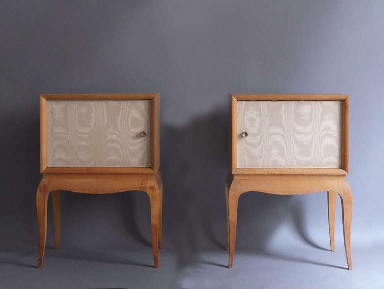 Pair of French 1950s of sycamore side or night tables with fabric covered doors and brass pulls.
 
