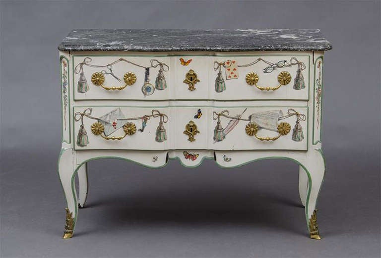 MAISON JANSEN
Two-drawer breakfront commode with painted trompe l’oeil decoration and veined gray marble top. Raised on hipped cabriole legs with gilt bronze hoof sabots. The whimsical painted surface includes playing cards, tassels, a key,