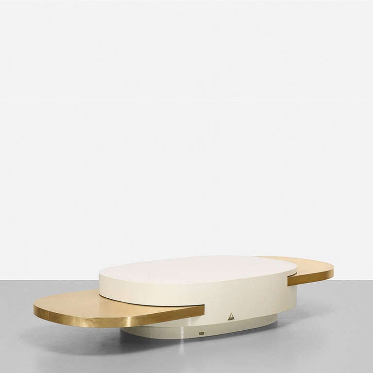 Gabriella Crespi (b. 1922).
“Elisse” oval coffee table in ivory lacquered wood with brass details. Sides feature pull-out brass shelves at staggered heights that give the table a metamorphic quality. Table measures 101 inches when fully