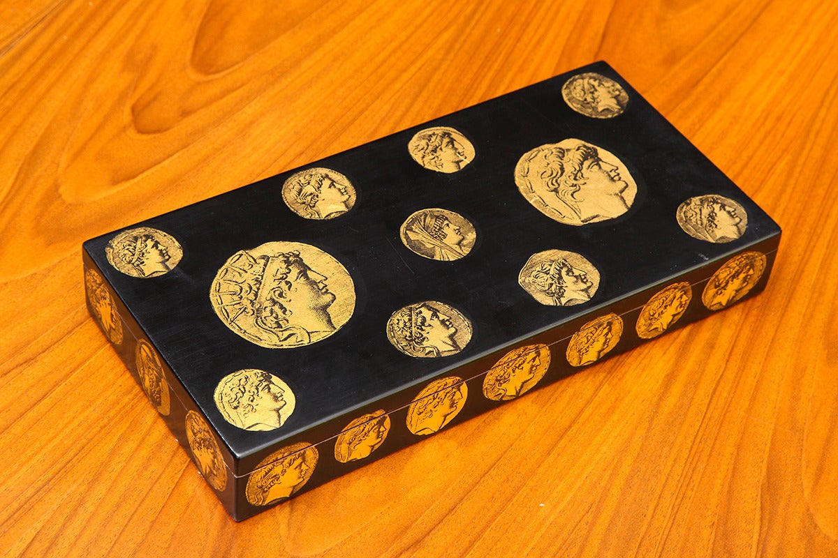 PIERO FORNASETTI (1913-1988)
Rectangular box in black lacquered wood with classical coin decoration in gold on the lid and sides. The interior is lined with faux malachite printed paper. 
Marked on bottom: Fornasetti Milano, Made in Italy