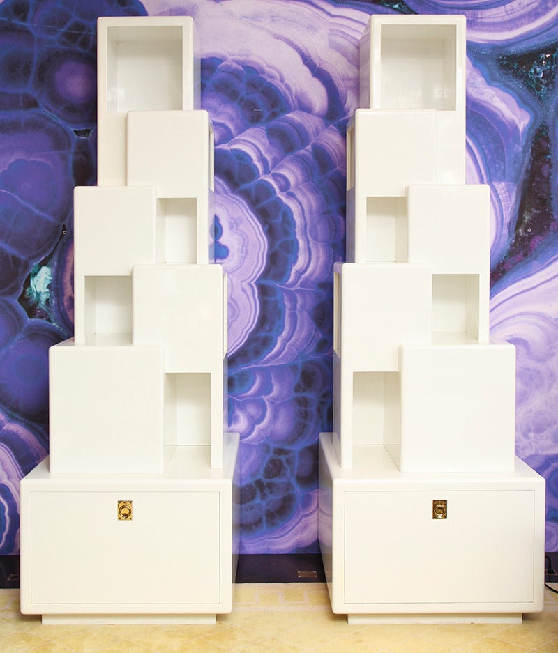 JOHN DICKINSON  (1920-1982) 
Pair of “Skyscraper” bookcases in wood with white lacquer finish. 
Each has illuminated side shelf and drop front doors storage space with brass pulls. These bookcases commissioned by Philip Schlein, the CEO of Macy’s,