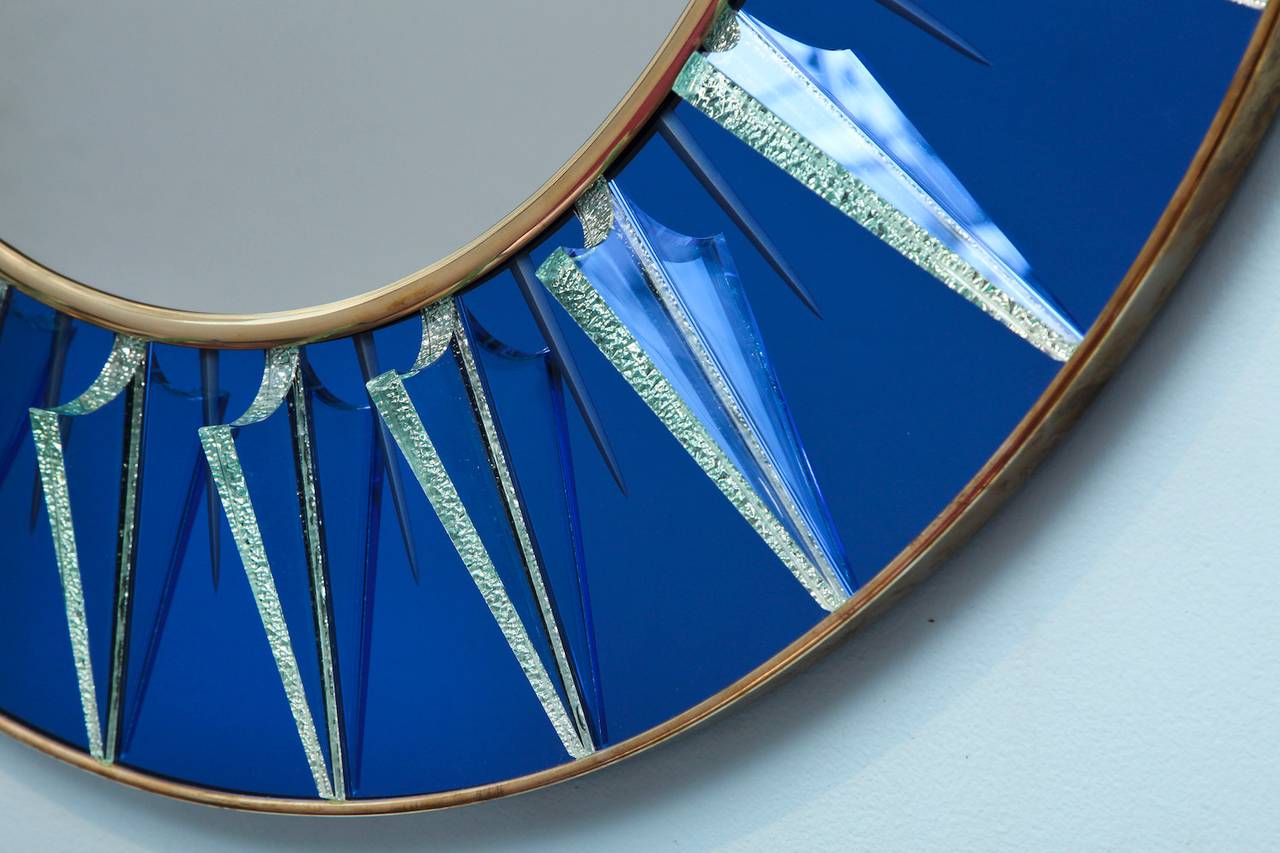 Large circular form with reverse cut blue mirror and relief-cut clear glass rays with foil backing. Center mirror and brass mounts. Signed on side edge. This piece was created exclusively for Donzella. These mirrors are made to order and require