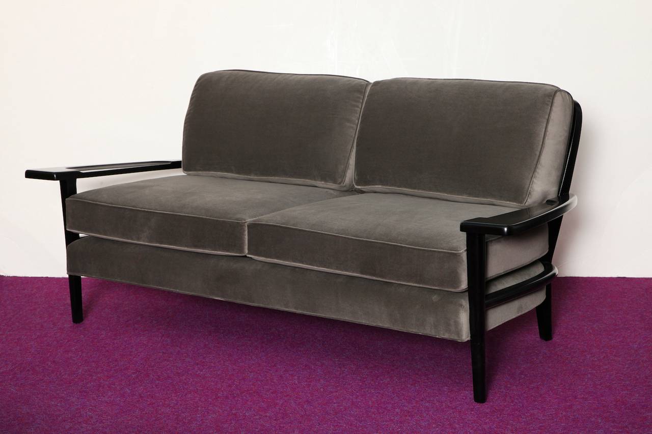  Rare plank-arm sofa by Paul Laszlo.  Sculptural sofa of ebonized wood frame. Wide plank arms with shaped cut-out sections. Curved back with spindle fret-work and tapered legs. Recently upholstered with a gray velvet. Very rare sofa version of one