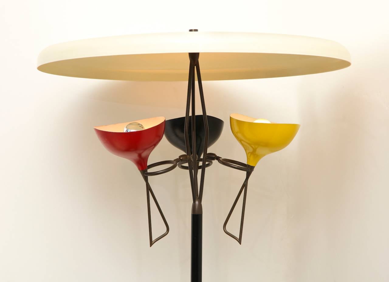  Three-light floor lamp by Stilnovo. Fantastic floor lamp with black-painted metal standard and shades in three colors. Shades with patinated brass mounts, that swivel and turn in all directions. Overhead off-white metal canopy reflector, and white