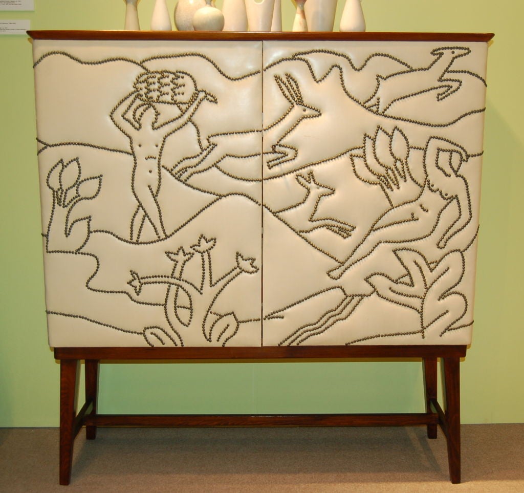 Unusual custom made cabinet with 2 adjustable shelves in birch. The exterior is covered in naugahide with paradise scene depicted in brass nailheads.