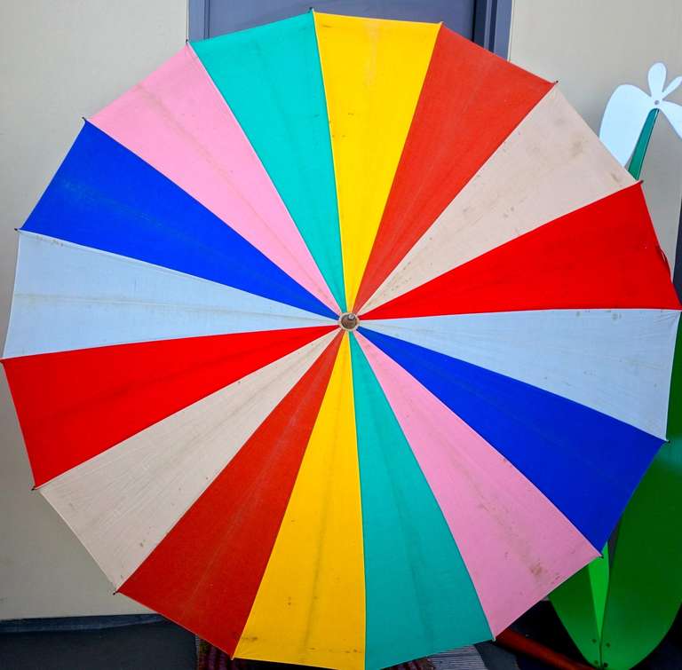 A delicious reminder of a gentler, more leisurely past. A wonderfully colorful pinwheel-like canvas umbrella with original carrying case and wooden handle.