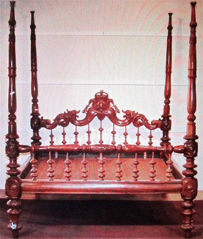 Large British Colonial mahogany four post bed, with spindle and openwork and crown carved headboard, four carved and turned tall posts with removable top sections, original rails and turned legs.
