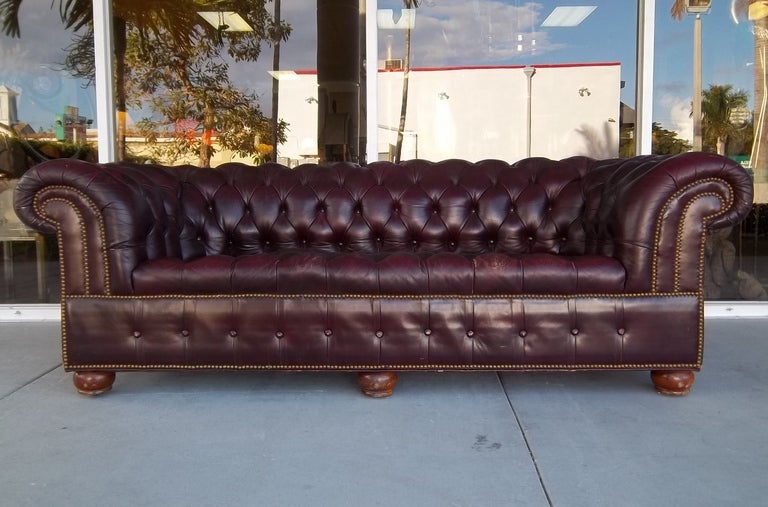 A classicly styled leather chesterfield sofa. This sofa is of a rich burgandy color and highlighted with brass studs. The leather is worn in spots but as with these sofas it only adds to the richness and beauty of this sofa. The sofa is deep and