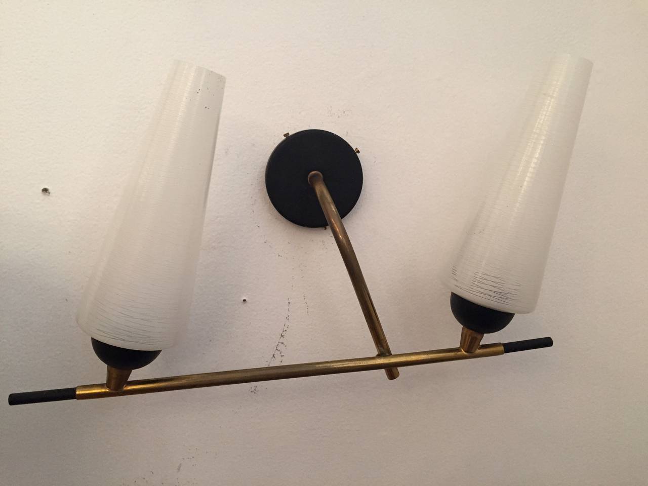 A pair of 1960s Italian Mid-Century wall lights composed of a polished brass and black enamel fixture with frosted and clear glass tube shades. Rewired.