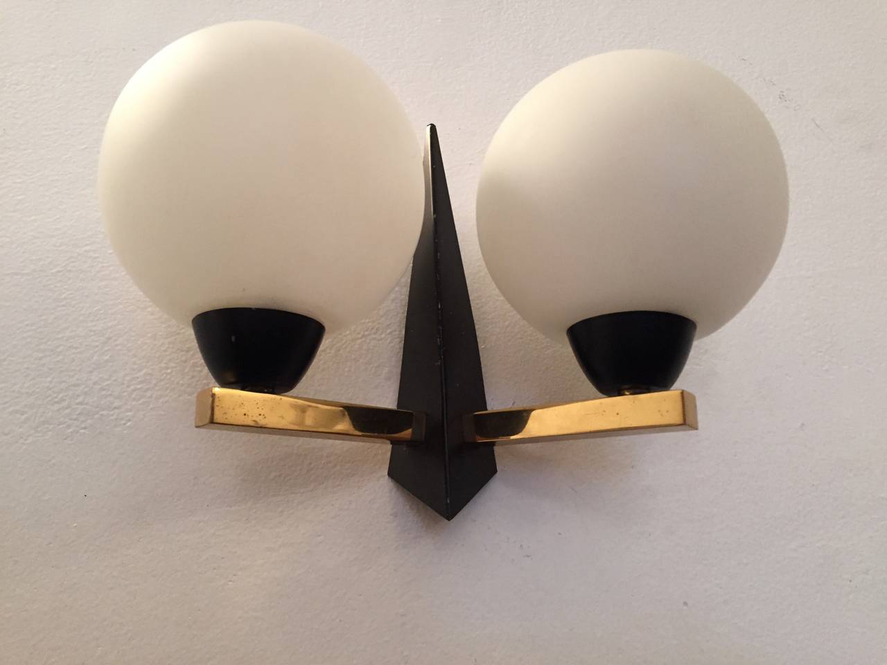 A great pair of original 1950s French Mid-Century sconces. They are composed of a black enamel and polished brass frame with two white glass globes. Rewired.