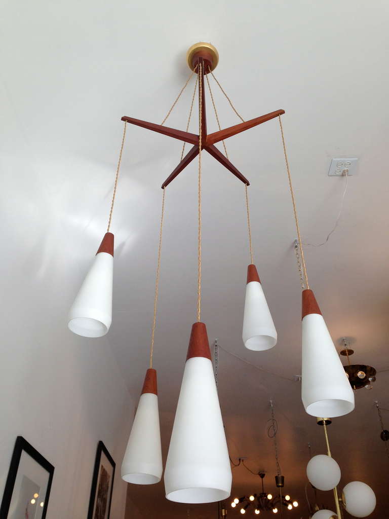 A wonderful "Mid-Century" 1950s Dutch chandelier composed of a teak stretcher, rayon cords, milk glass shades, and teak caps. Rewired. The height can be adjusted if needed.