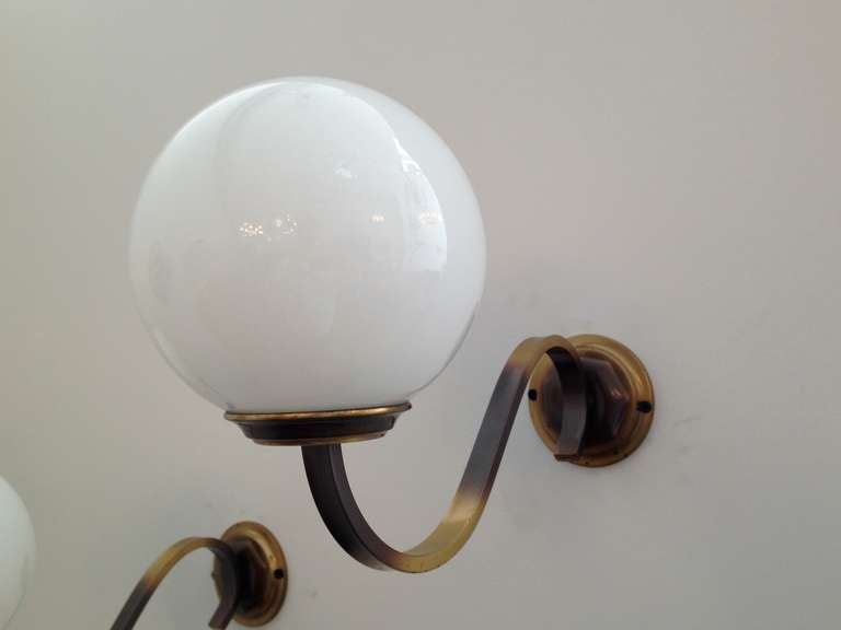 A pair of  Art Deco sty;e 1970's German wall lights with aged brass curved fixtures holding white glass globe shades.