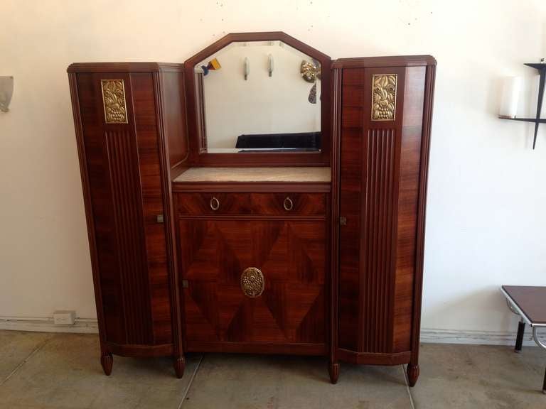 An amazing large 1930s French Art Deco cabinet with doré bronze decorative pulls and medallions with a built-in mirrored bar cabinet. The cabinet has fluted feet with a marble top and center mirror. Two of the gilded bronze medallions have a