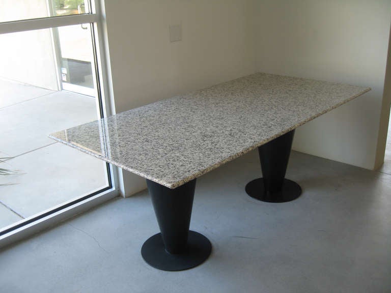 . The table was designed in 1983 and has black enameled steel cone shaped pedestals and a black/tan/white confetti granite top. The table is an excellent example of early eighties design.