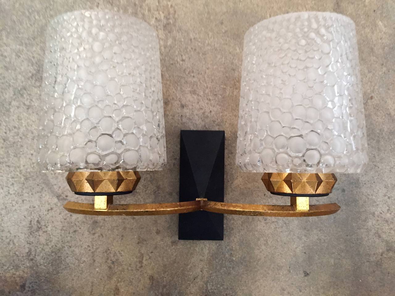 A luxurious pair of 1960s French sconces composed of a matte black and gold leaf body holding lightly frosted thick bubbled glass shades. Rewired.