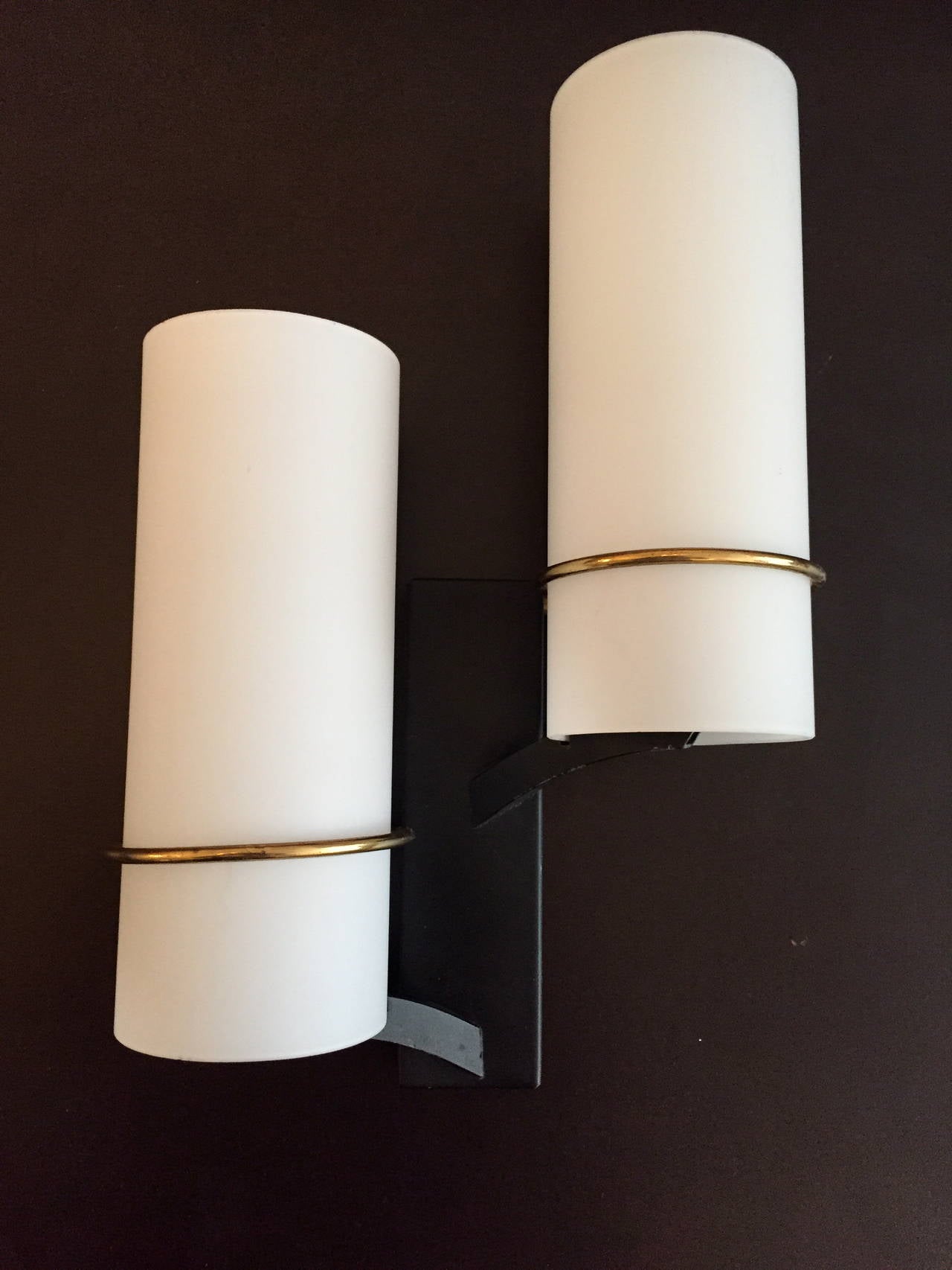 A wonderful pair of 1960s French sconces done in matte black enamel fixtures with polished brass rings holding frosted white glass cylinder shades. Rewired, by Maison Lunel.
