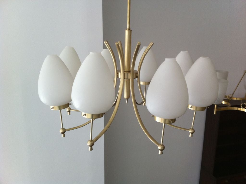 A grand eight light swooping chandelier by the Italian maker, Stilnovo. Eight frosted egg shaped glass shades on a satin brass fixture. The ceiling pole can be adjusted to your needs.