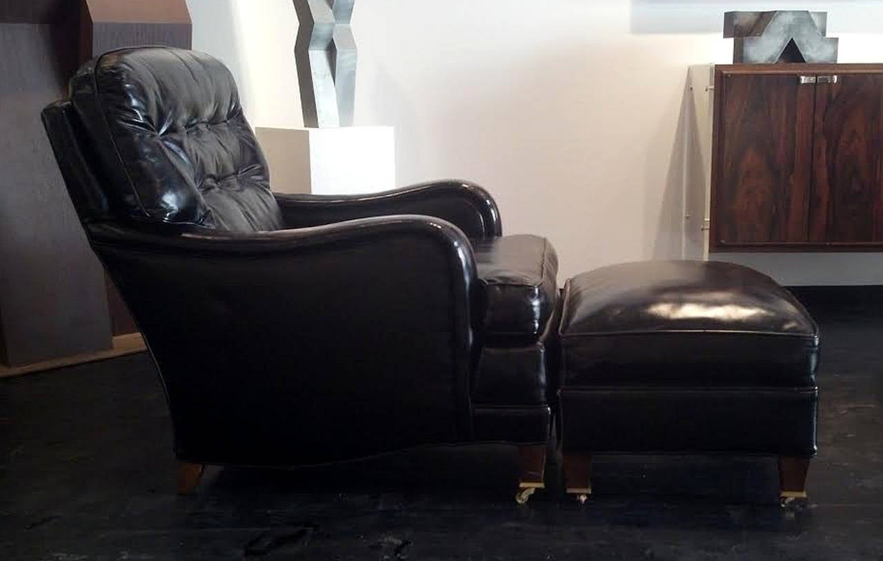American Art Deco leather club chair and matching ottoman in black burnished leather, tufted and buttoned back and walnut feet with brass casters. Minor wear to leather, amazing overall condition and patina. Very chic and very sexy, the black accent
